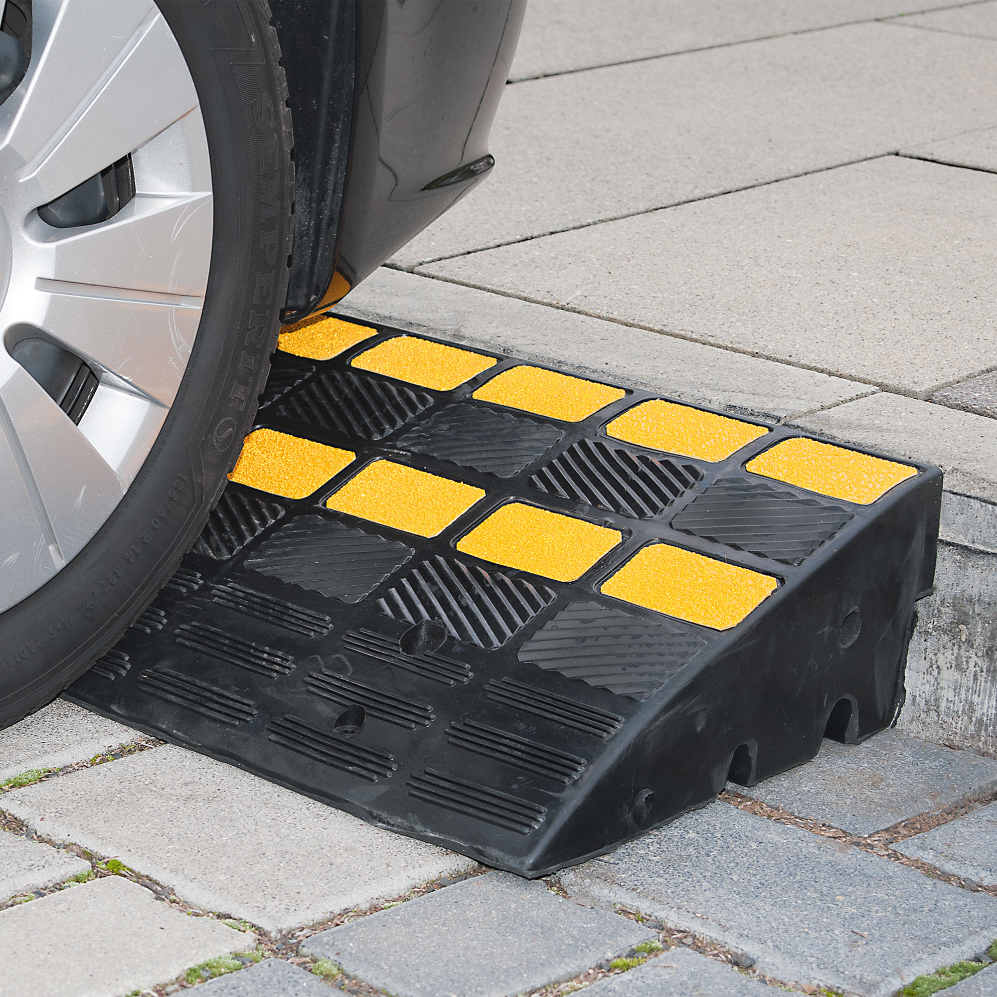 Zwarte verkeersdrempel met gele reflecterende markeringen voor voertuigen op een straat.